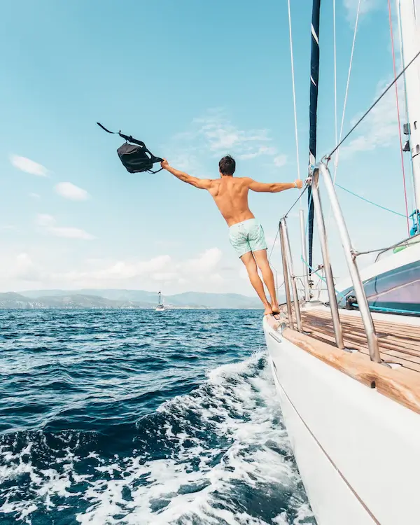 Man in swimming shorts, swinging off the side of a boat with a bag in his hand.