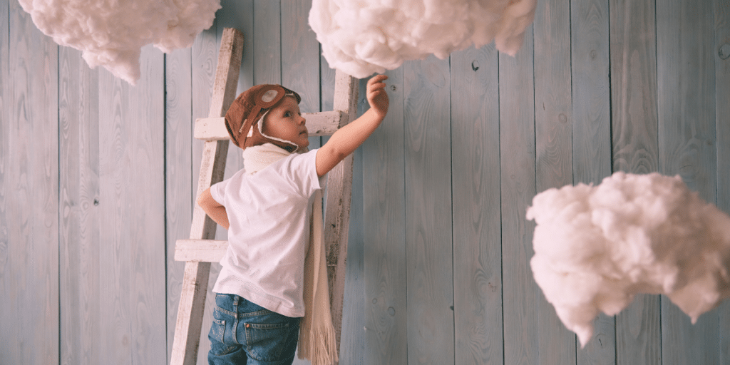 Goal Setting after 40: A young boy climbing a ladder reaches toward some clouds. Symbolizing that you need more than dreams, you need goals and a plan to get to your dreams.